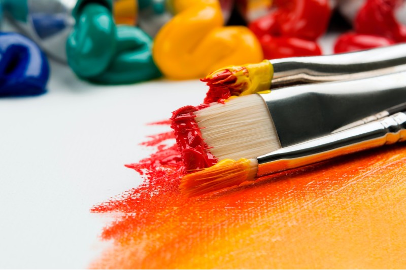 Photo of paint brushes and paints sitting on top of a blank canvas.