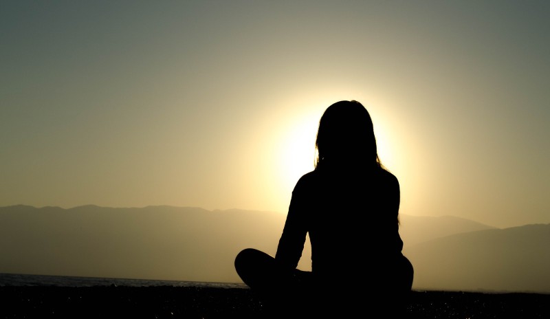 A photo of a woman practicing yoga and/or meditation in front of the rising sun.