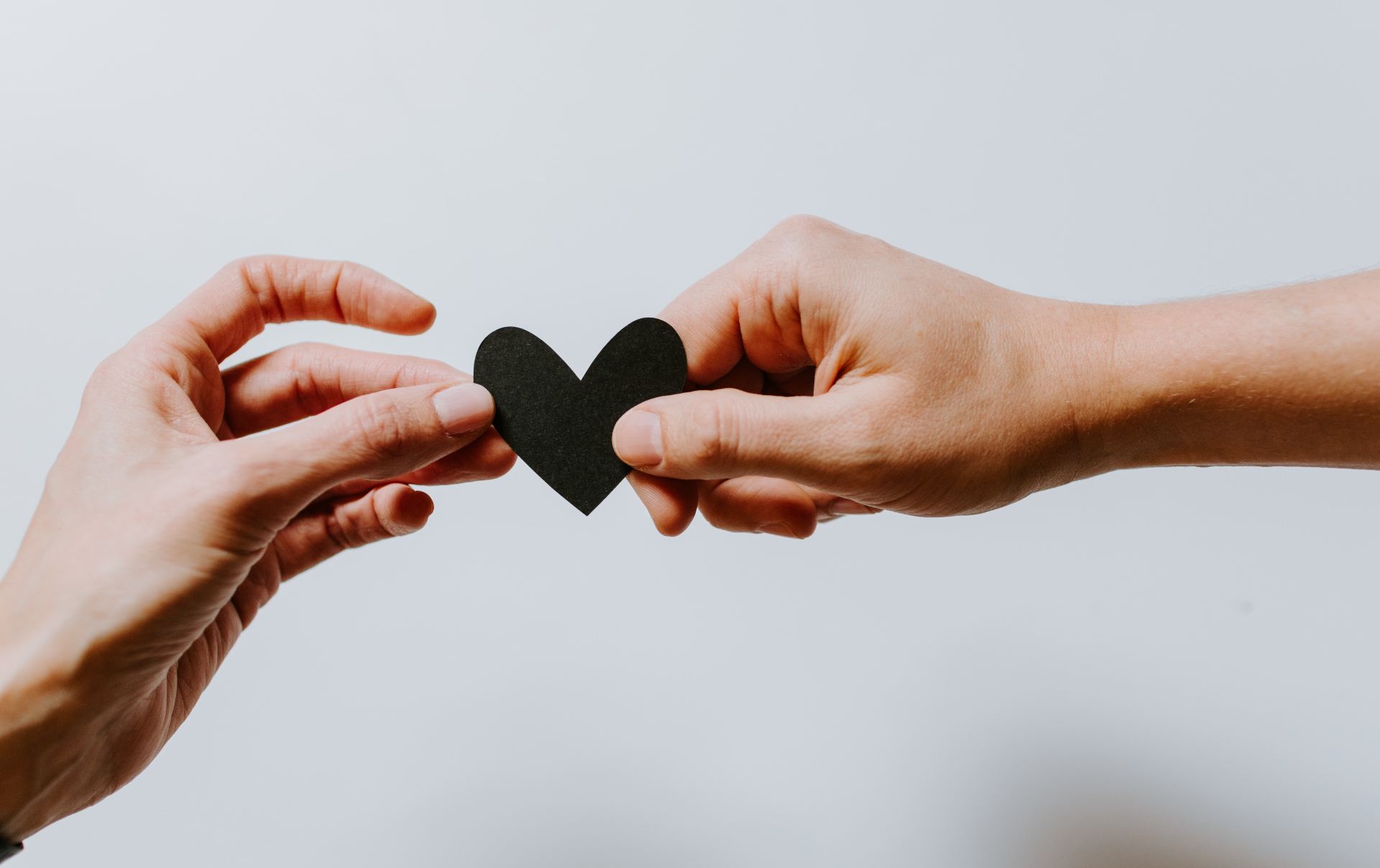 Photo of two hands holding a black heart together.