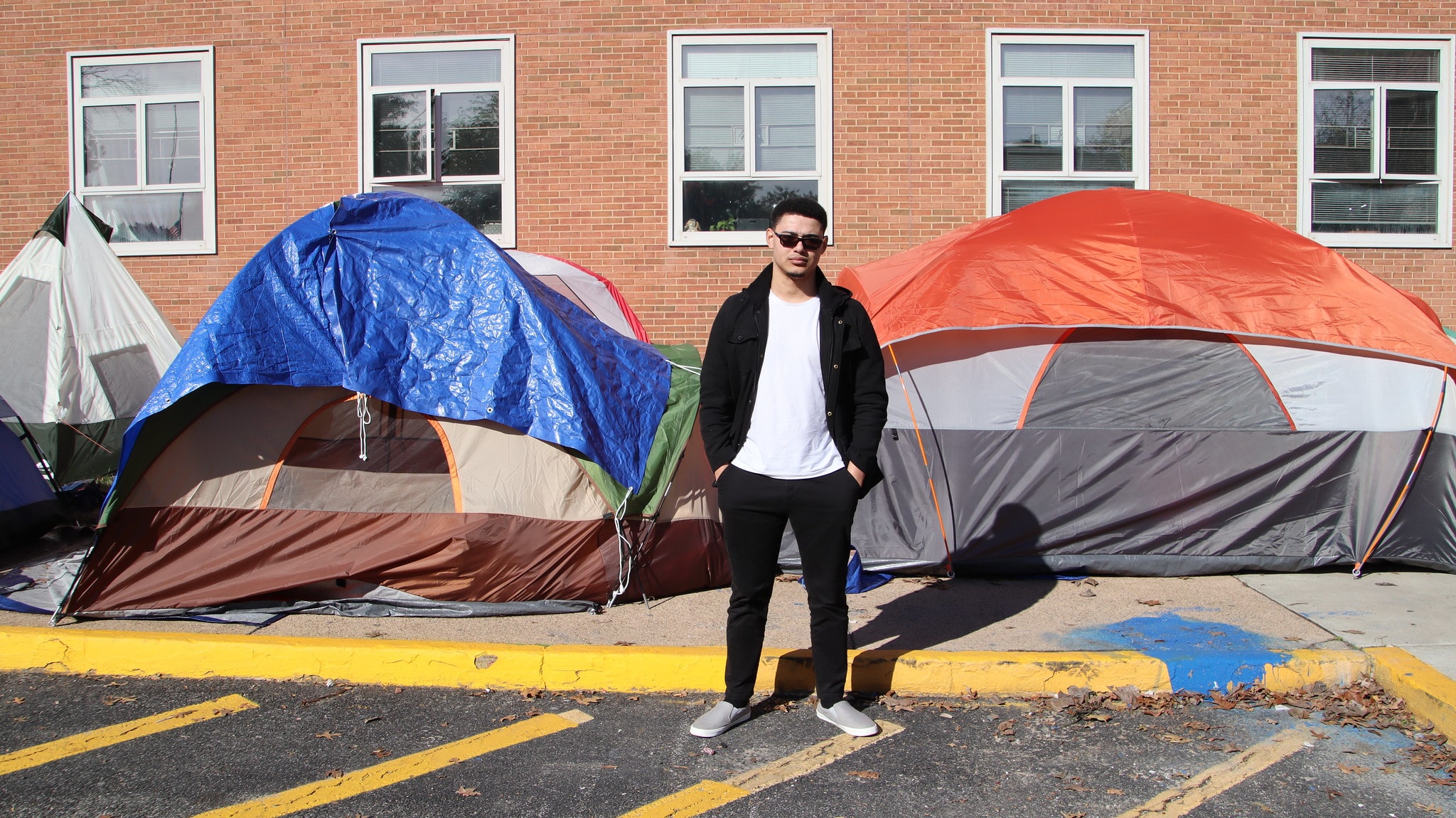 A young man stands in front of two tents on the side of the street.