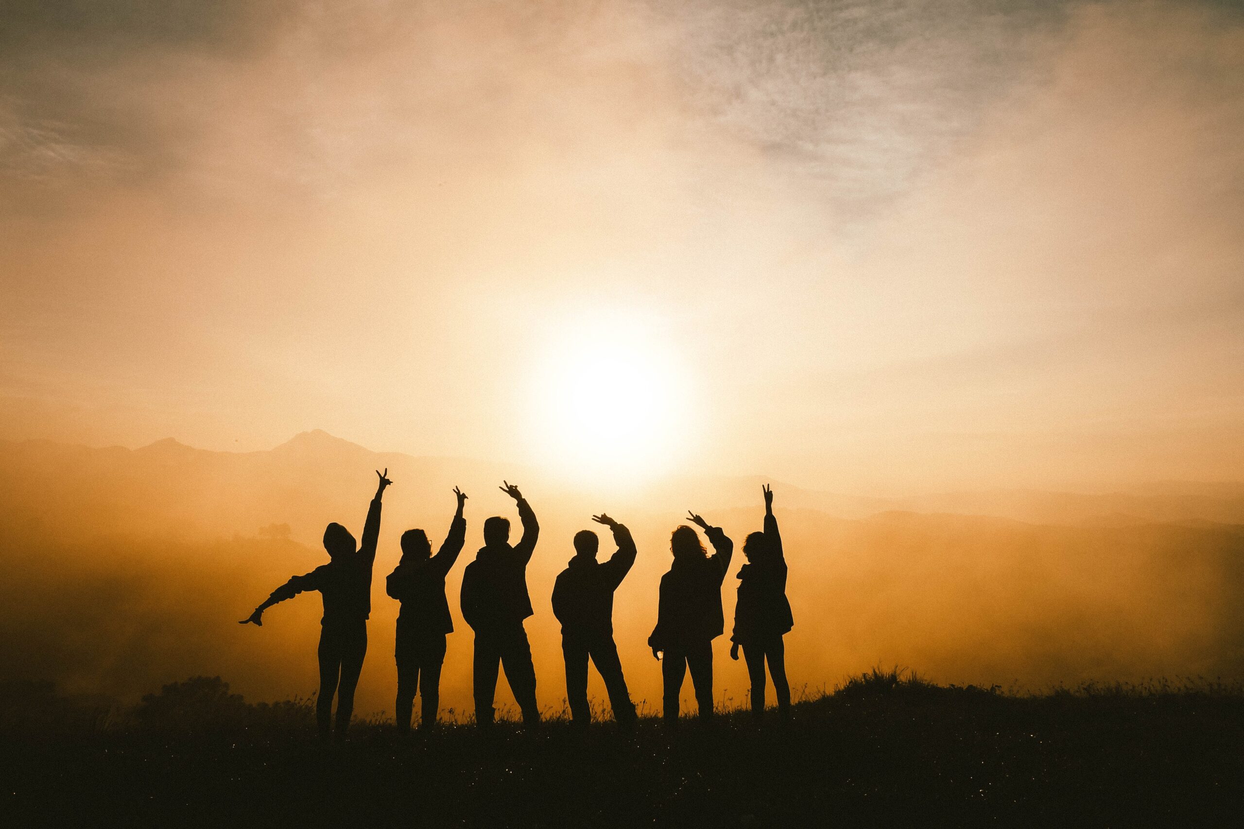 Photo of 6 friends who are backlit by a sunset.