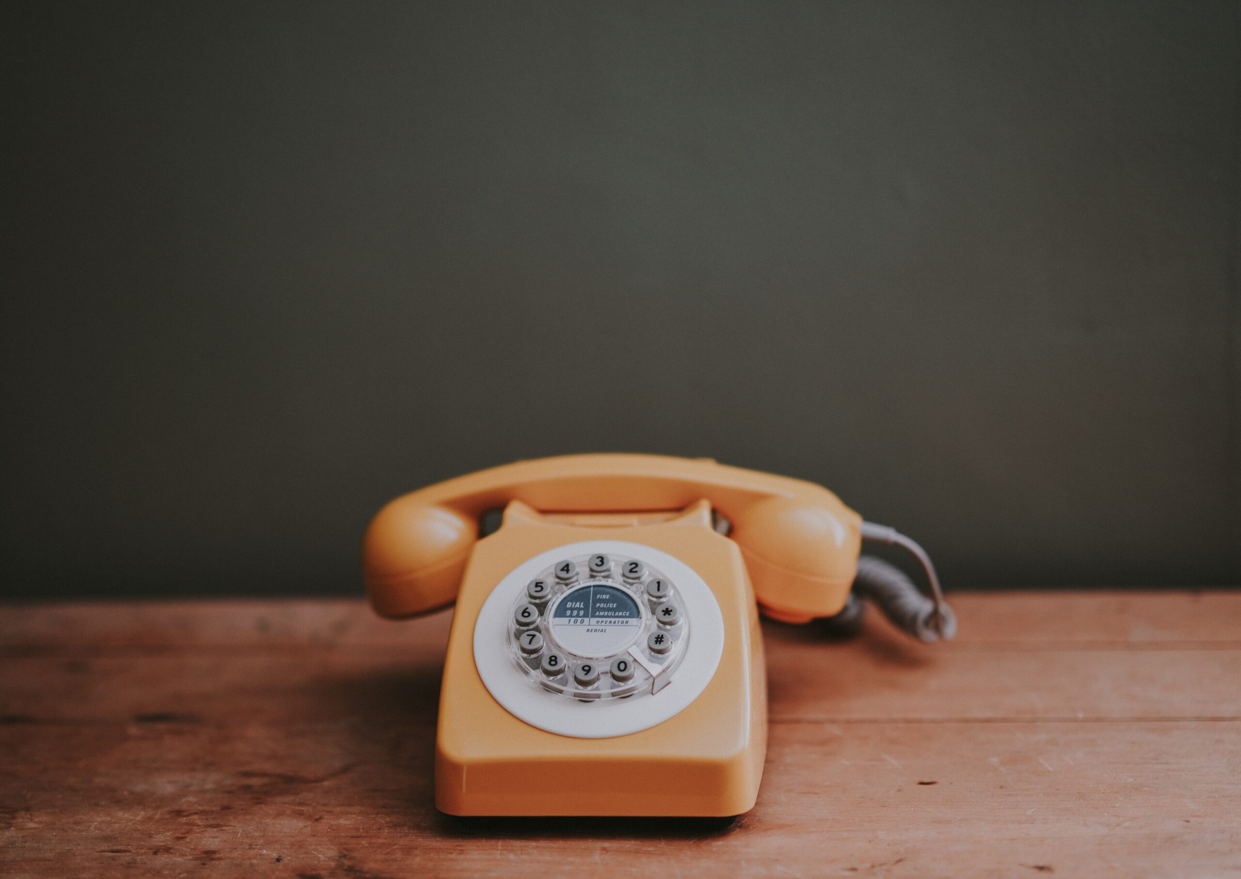 Photo of an orange landline telephone which is sitting on a wooden table.