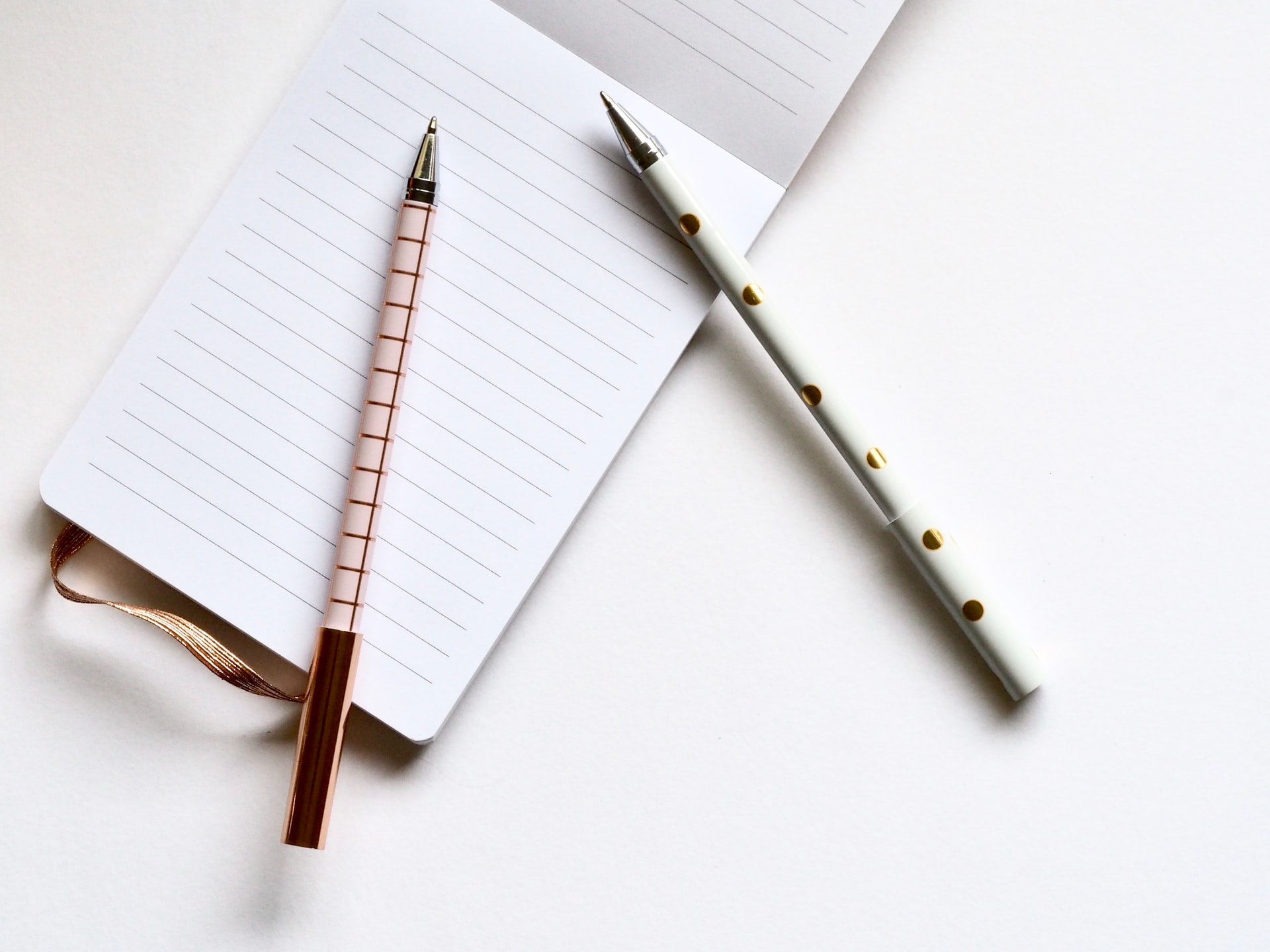 Photo of an open notepad with two pens laying on top. One ben is red with plaid stripes and the other is blue with polka dots.