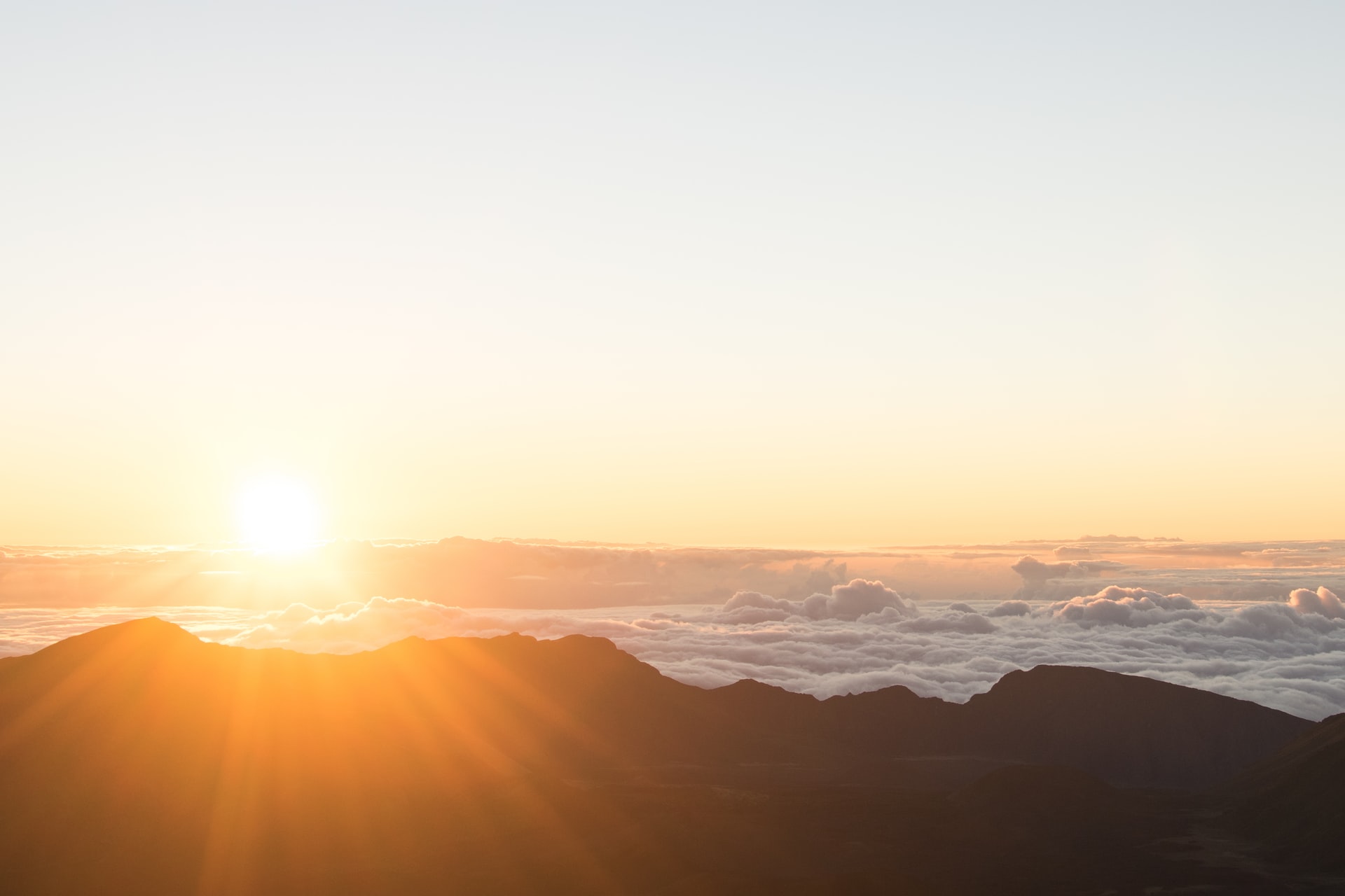 Photo of the sun rising over a mountain range covered in clouds.