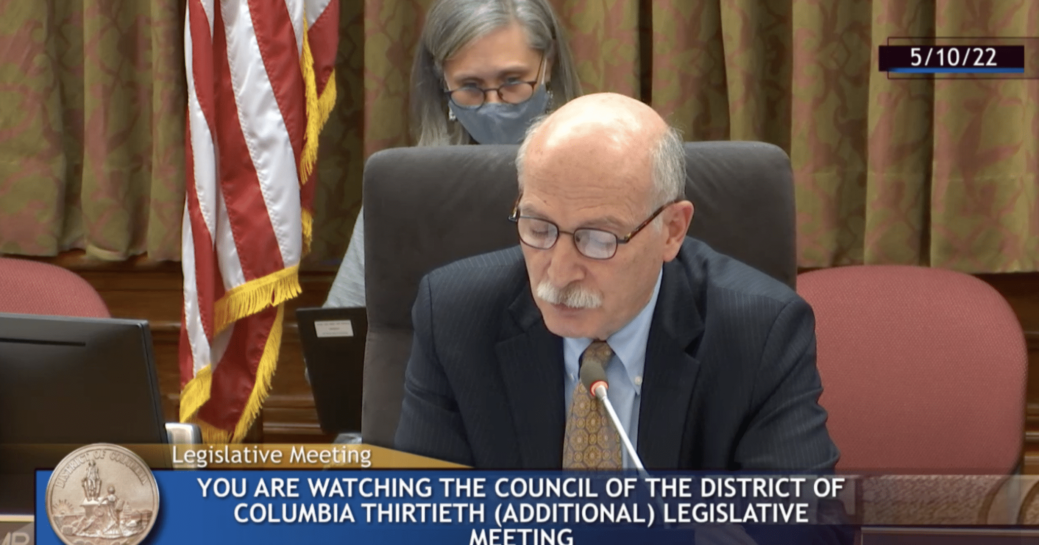 Phil Mendelson sits in a chair in front of a brown curtain in the D.C. Council chambers.