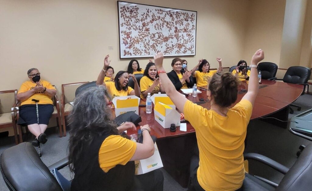 People in yellow shirts sit around a table cheering.