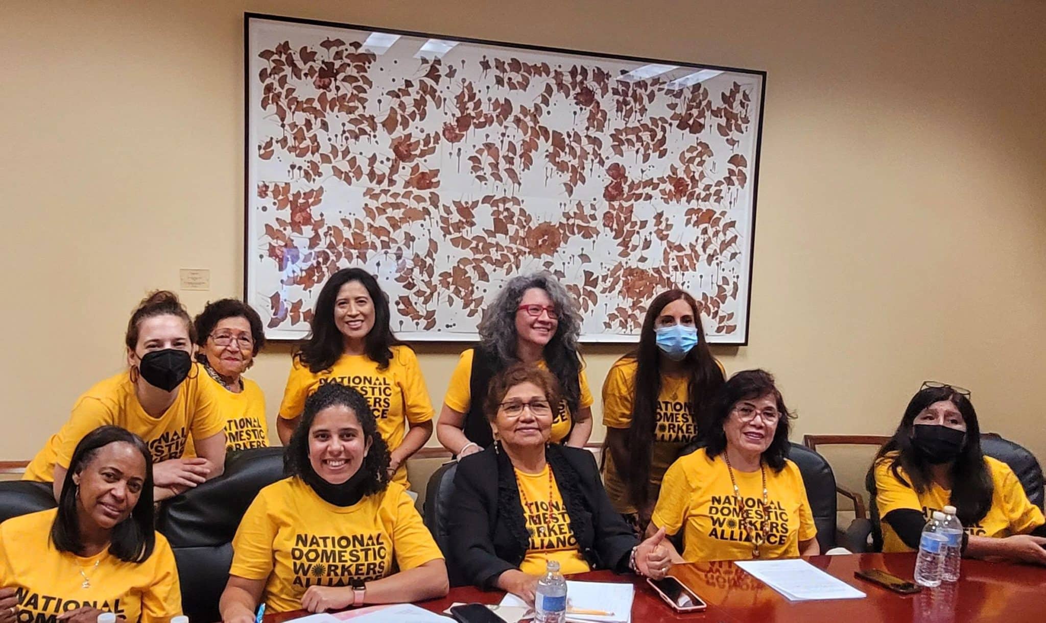 Women in yellow shirts smile in front of a table. 