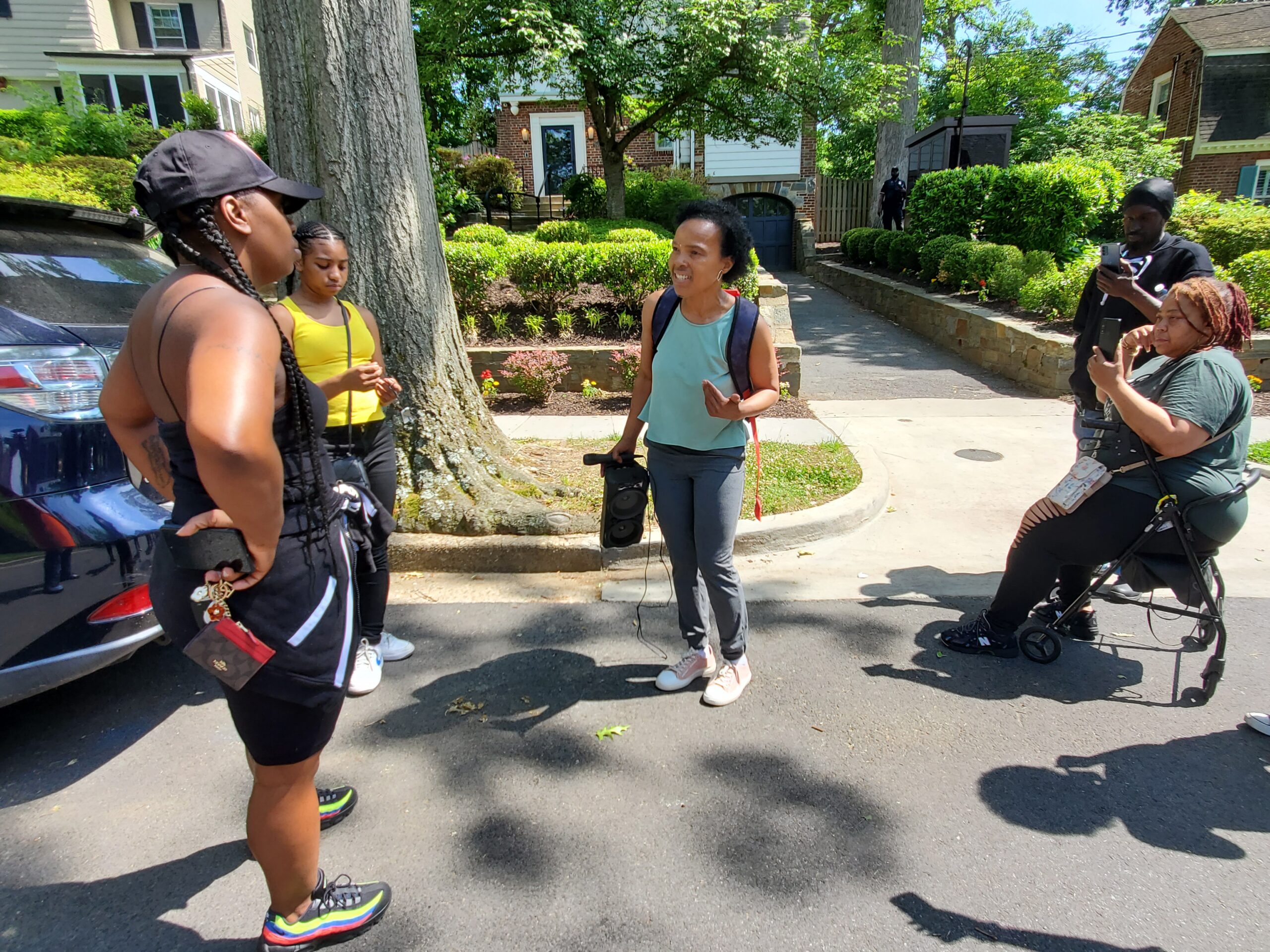 A group of Black, female-presenting people gather in front of a house on the street.