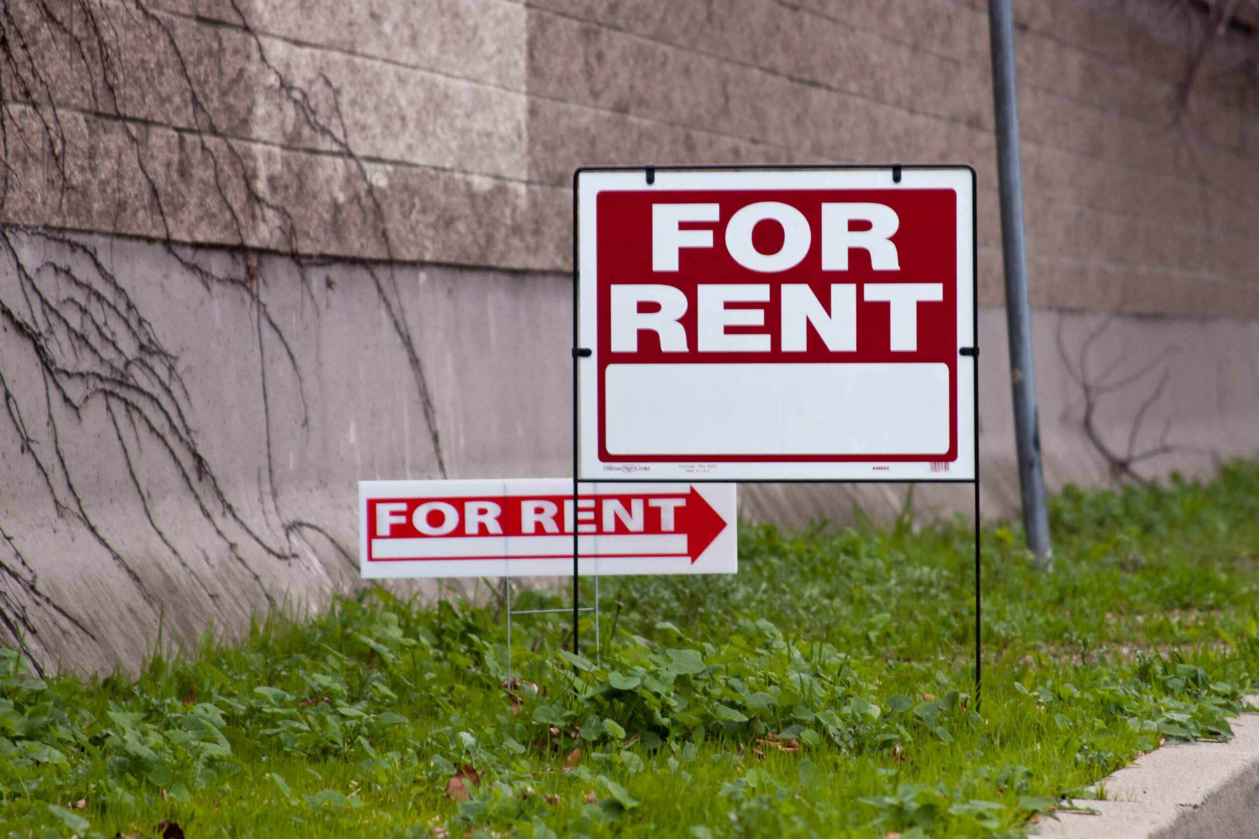 A white and red for rent sign in front of a brick wall. Housing voucher recipients can have trouble renting.