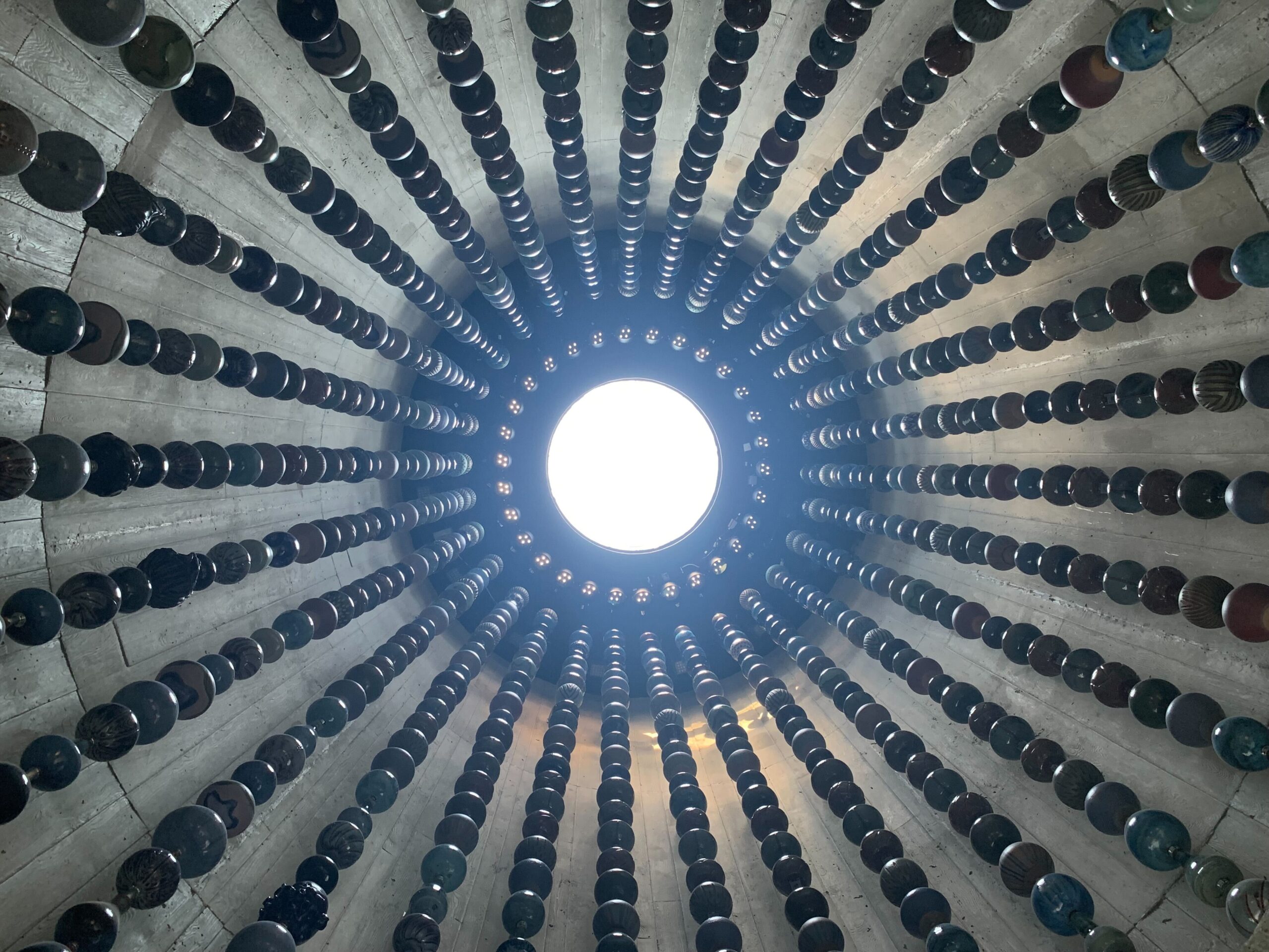 A circle of light chines from above into a round tower, with strings of beads hanging down around it.