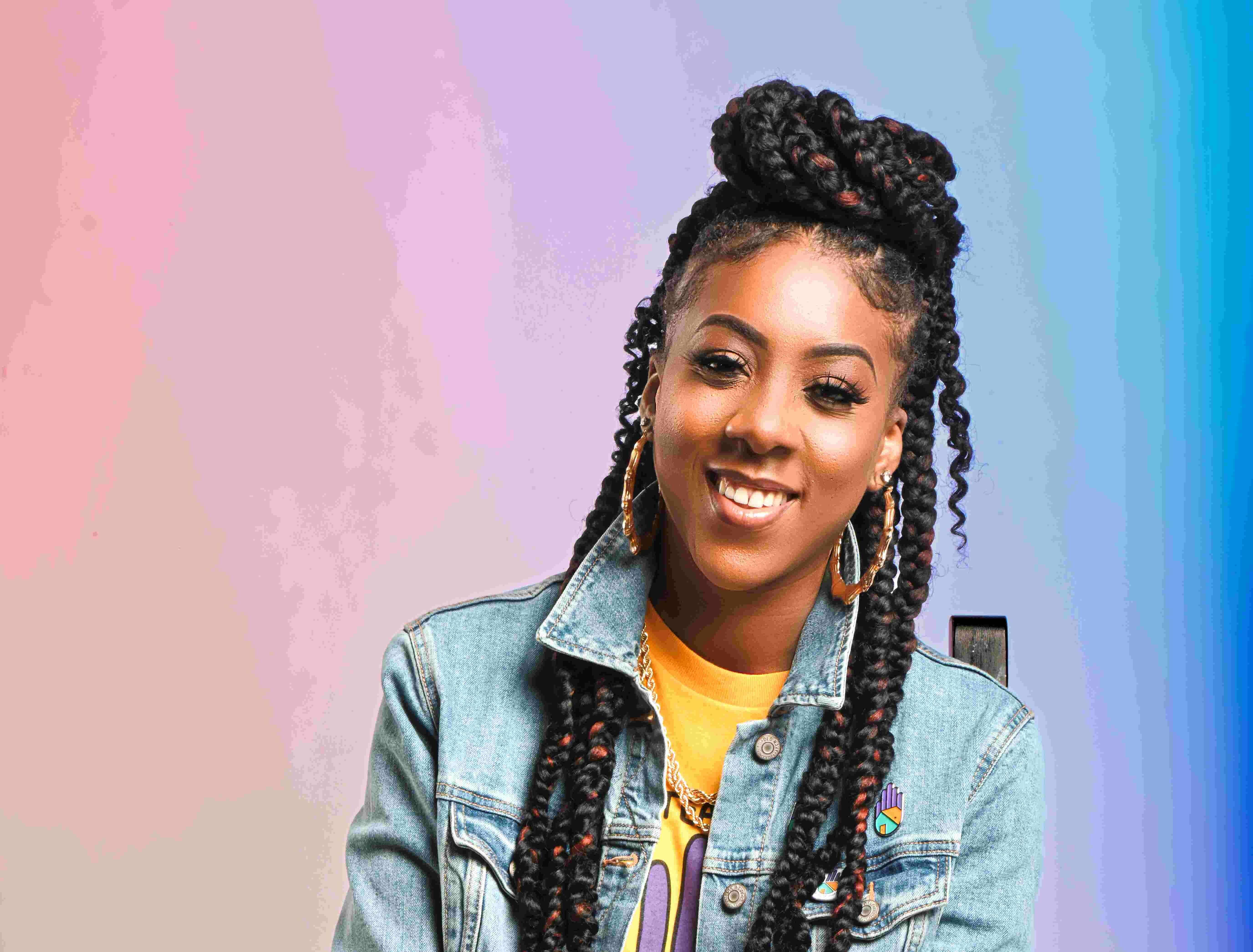 A young Black woman poses on a stool.