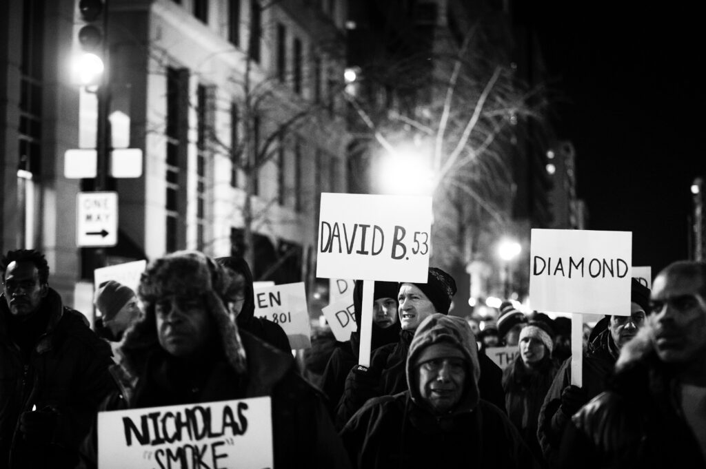 People march down the street holding signs remembering those who have died.