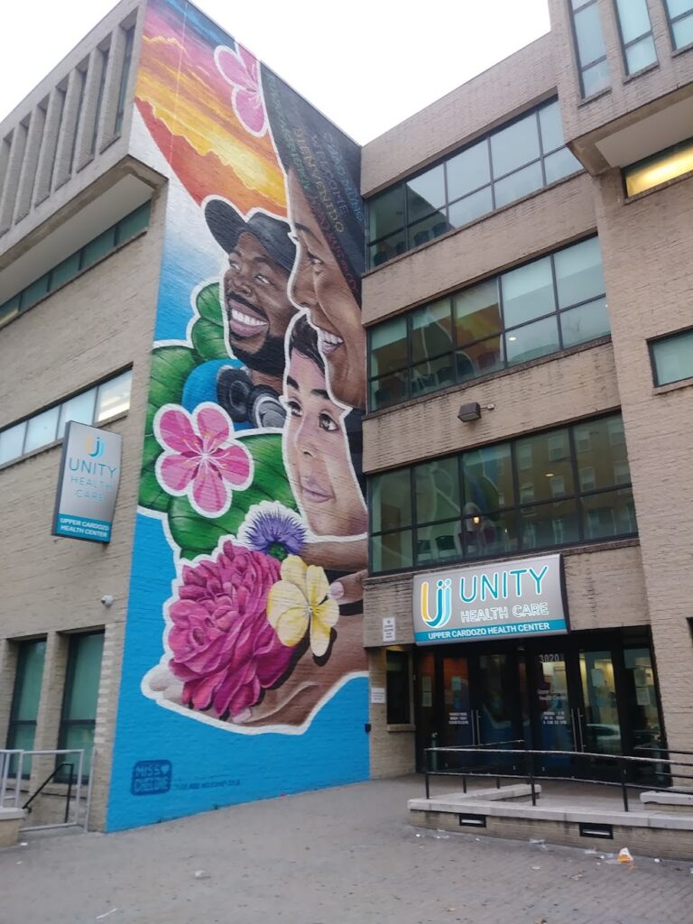 A blue mural with faces on a wall next to the entry to a Unity facility.