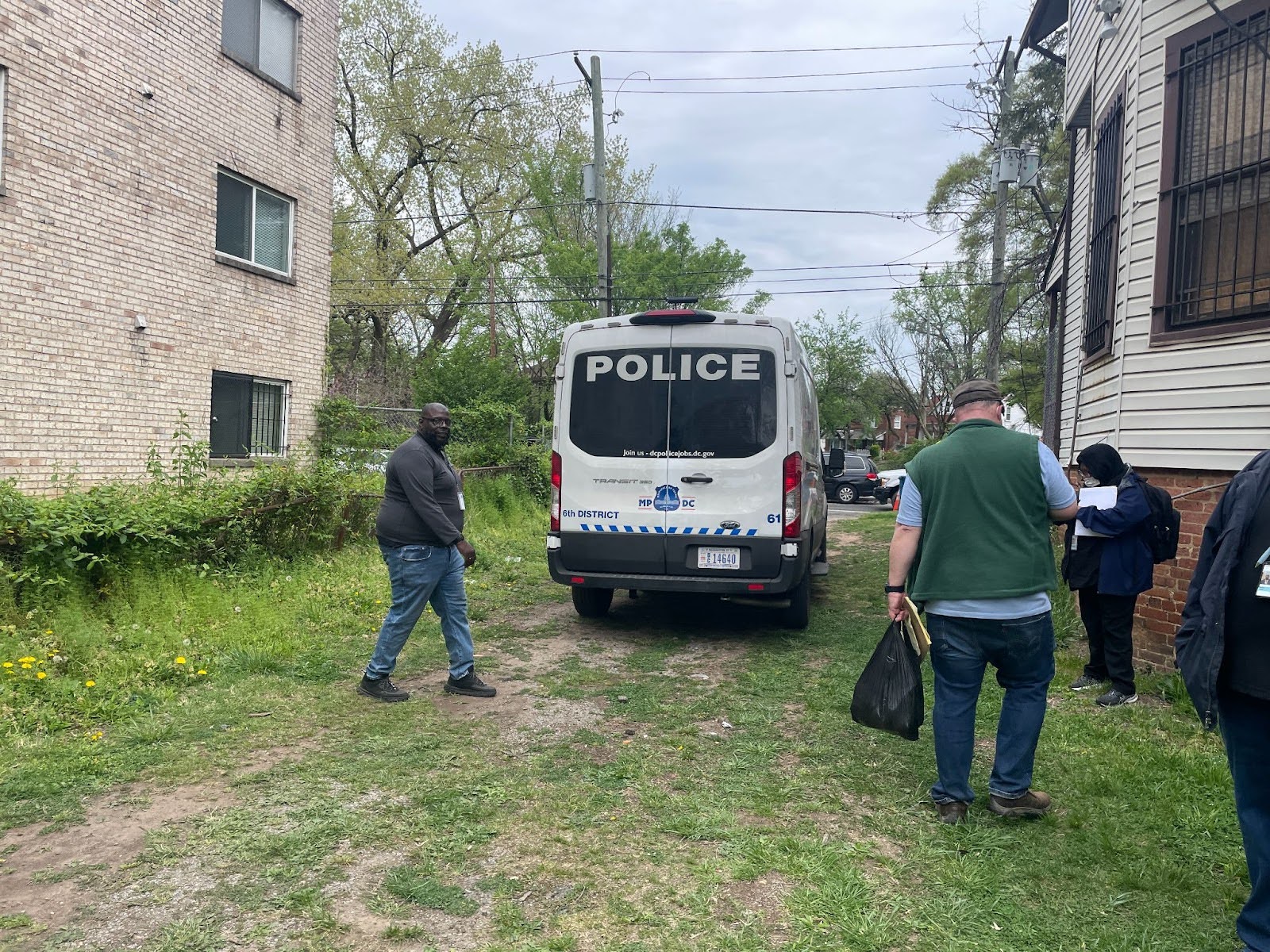 Two men stand by a police van parked on a lawn.