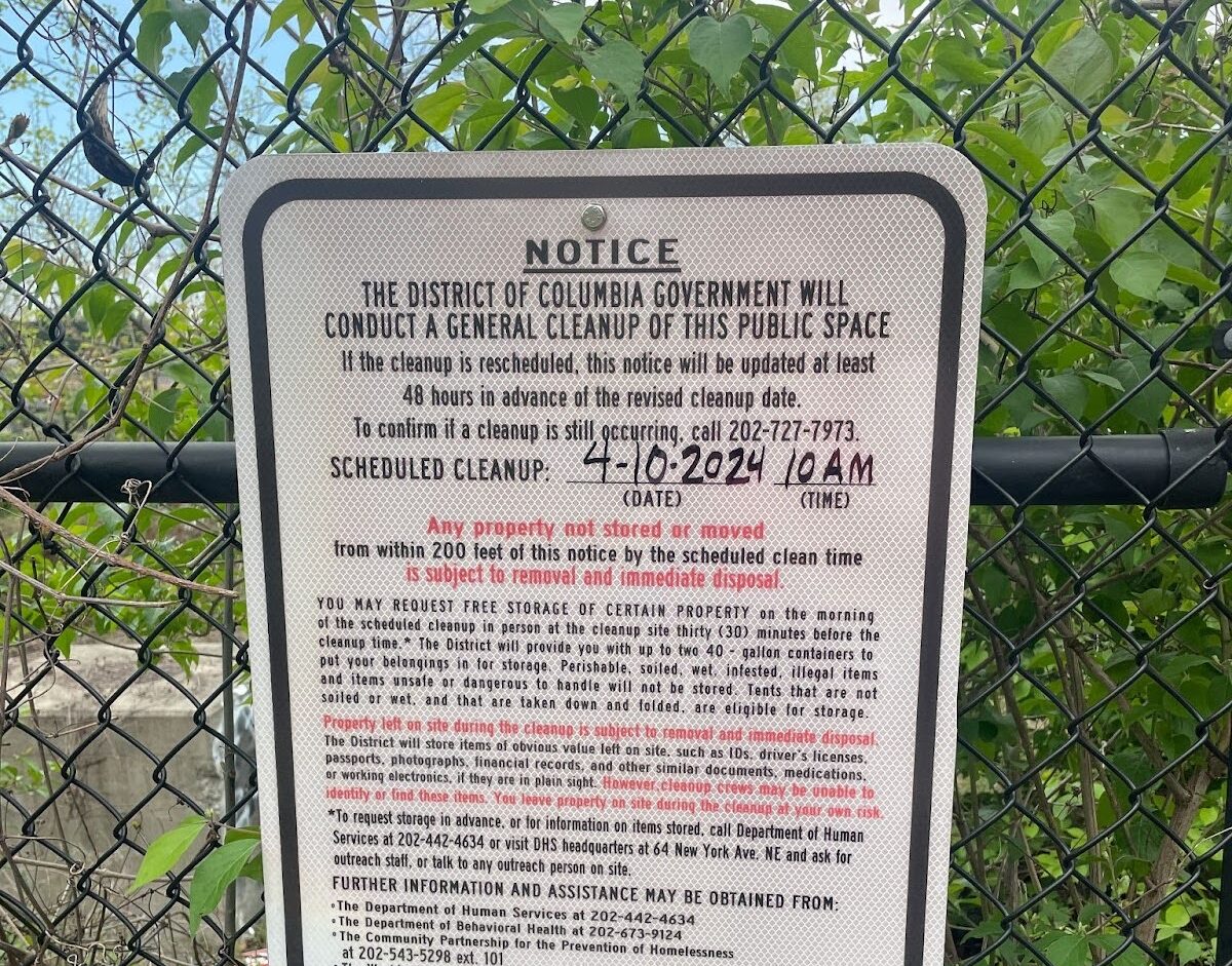 A white sign on a fence in front of trees.