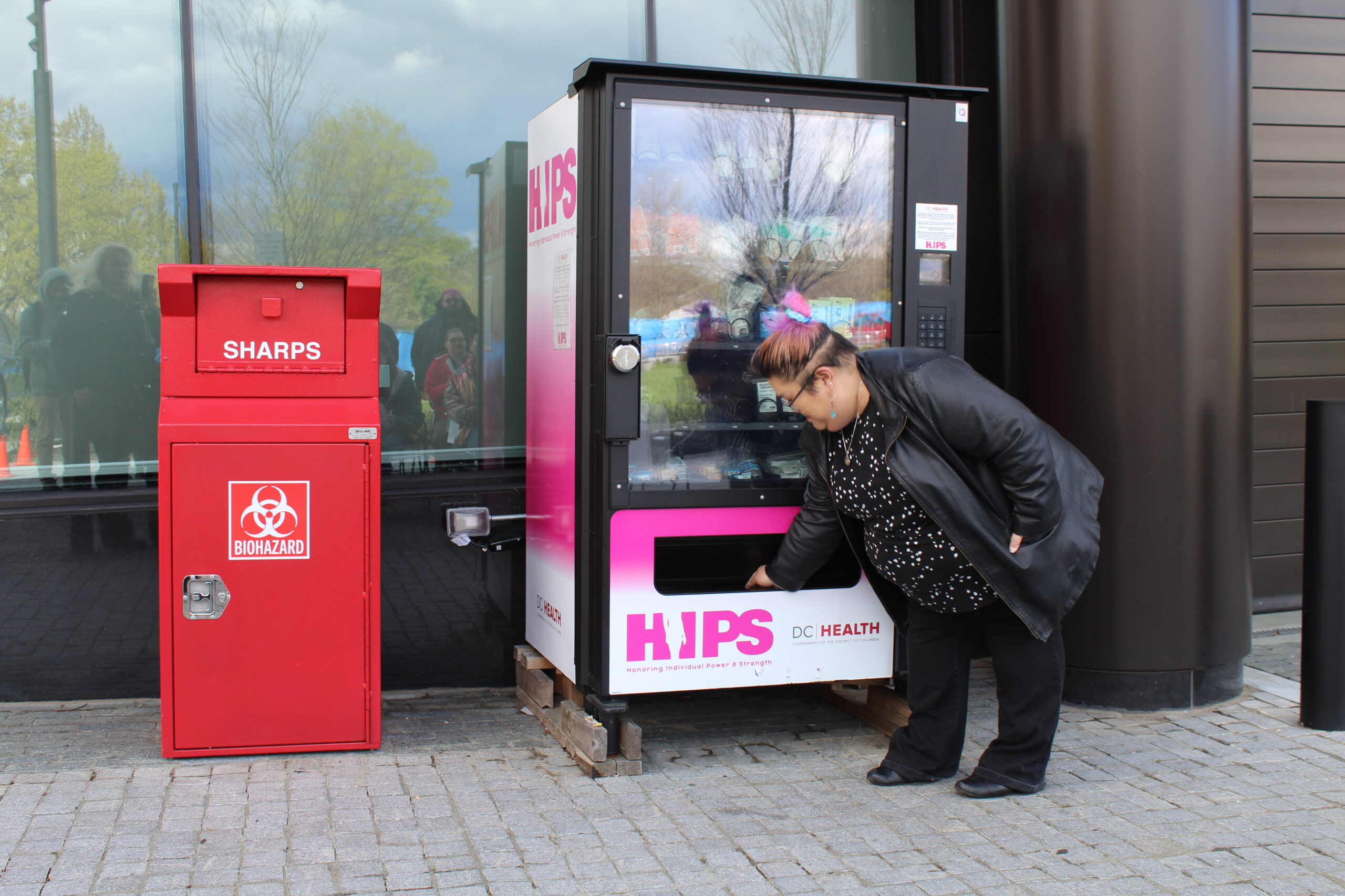 A person in all black leans down to take something out of a harm reduction vending machine.