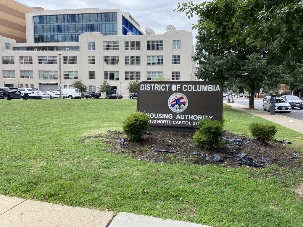 DCHA black sign on green grass behind a tan building. The DCHA recently addressed the 2022 HUD Report.
