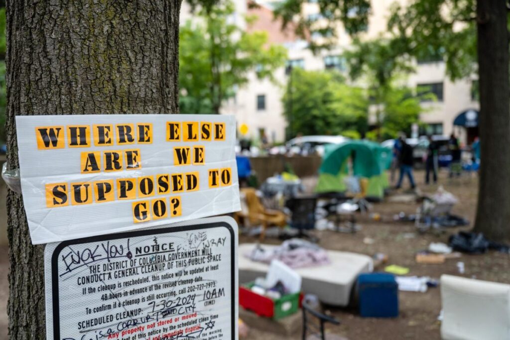 A sign reading "Where else are we supposed to go" tacked to a tree in an encampment.
