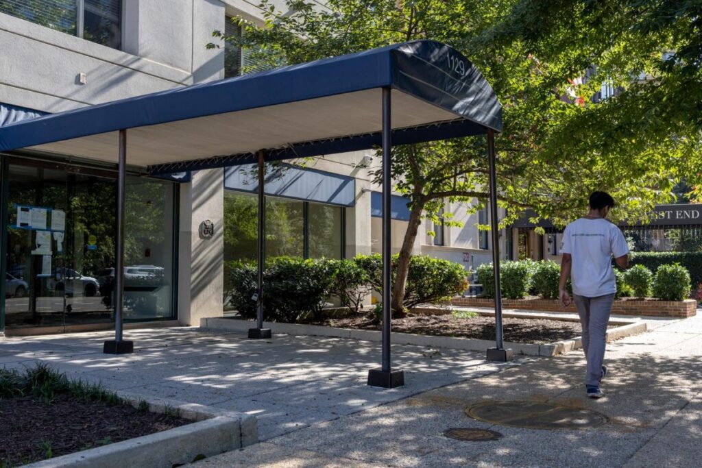 A man in a grey shirt walks by a blue awning.