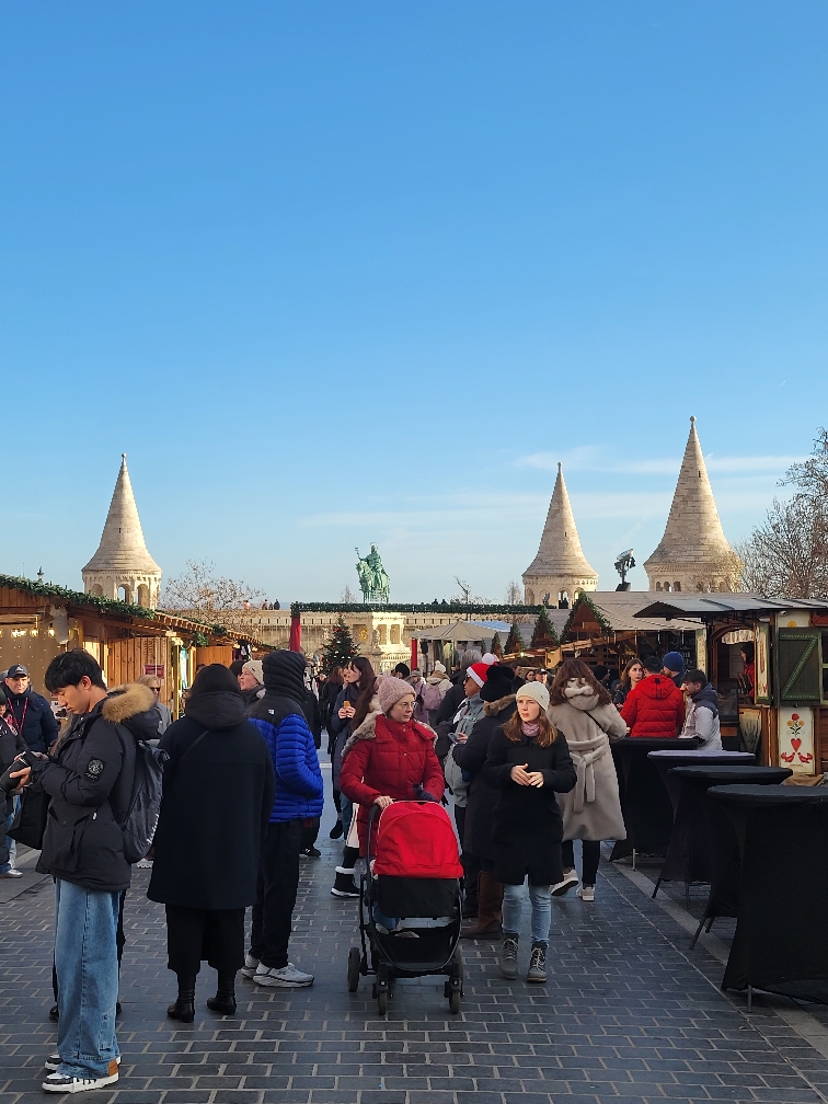 People walk in the center of a market under a blue sky.