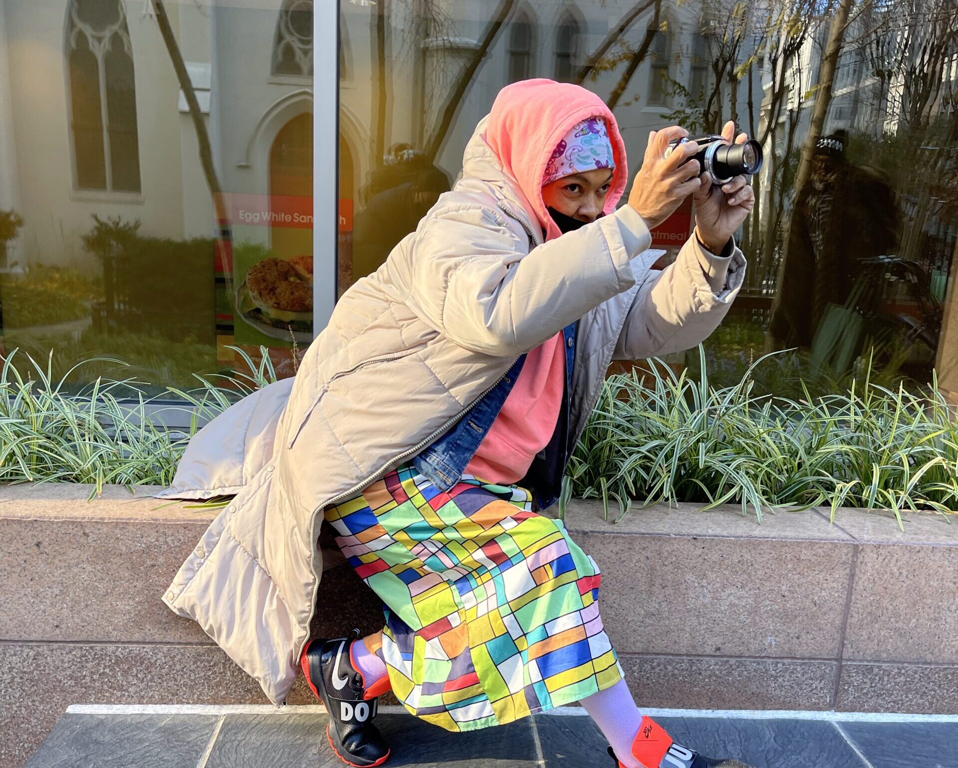 A Black woman in a multicolored skirt leans to her left to take a photo.