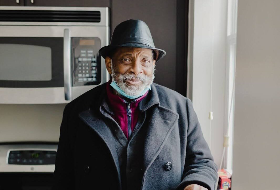 A Black man stands in front of his kitchen, smiling.