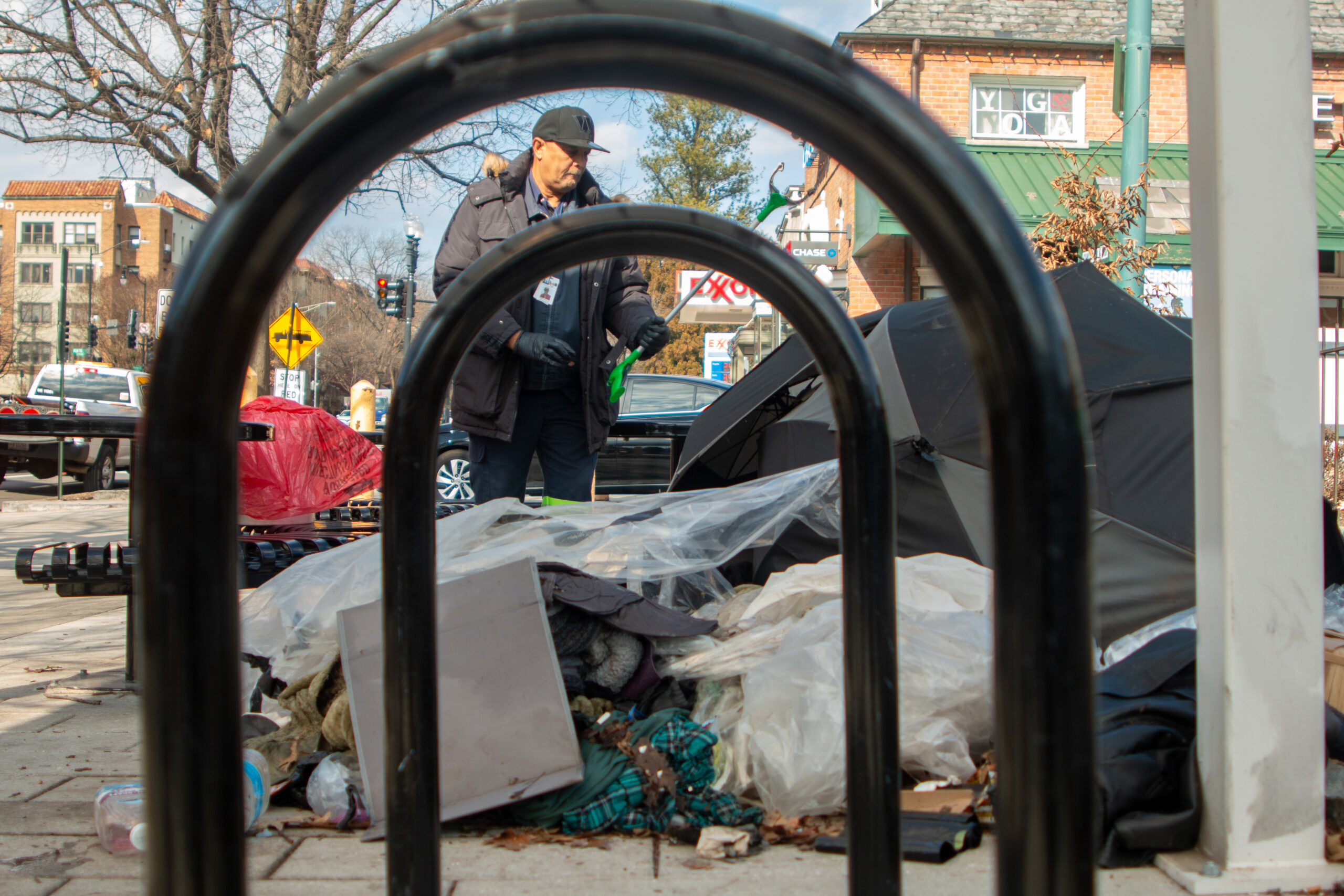 Through two black curved bars, viewers can see a city worker and encampments.