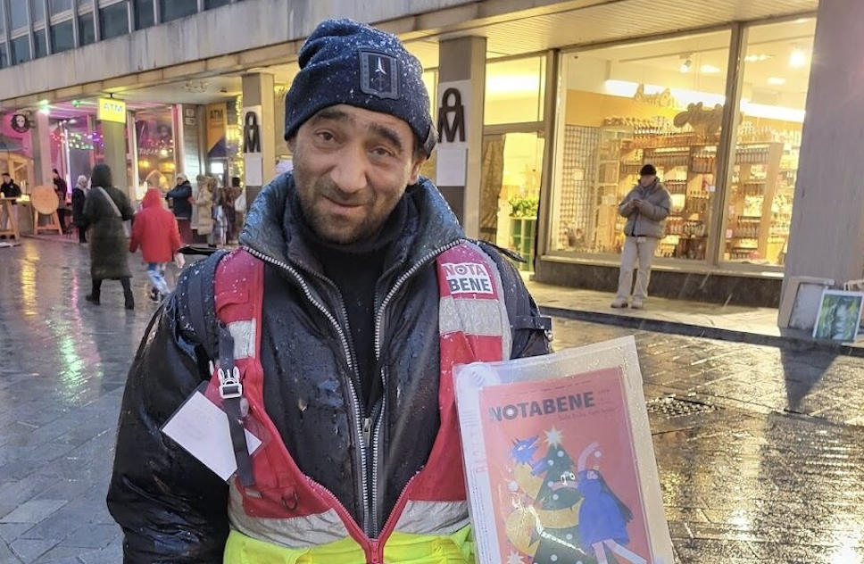 A smiling man holds up a paper in the snow.