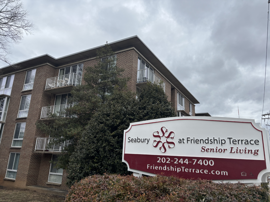 A brown apartment building with a red and white sign in front reading "Seabury at Friendship Terrace."