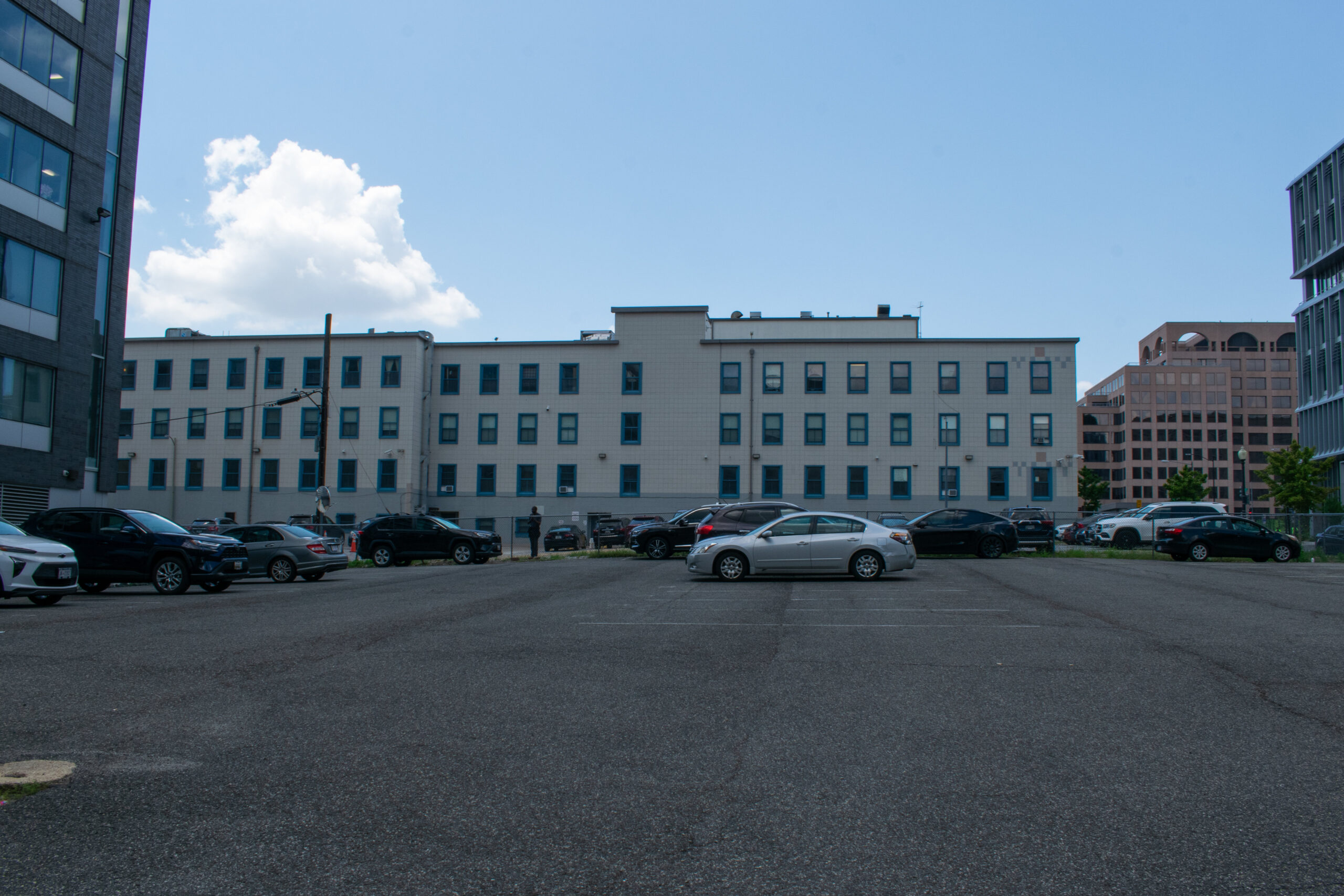 Across a grey parking lot, a long white building with blue windows.