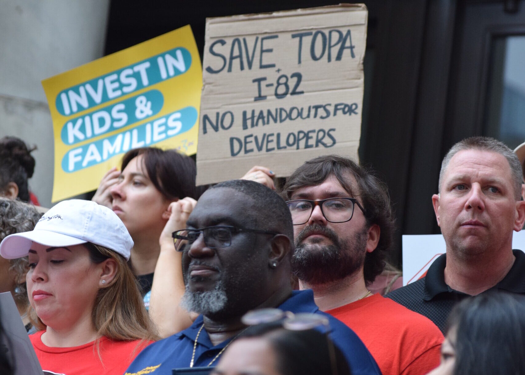 A crowd holds up signs calling for the government to "invest in kids and families" and "save TOPA."