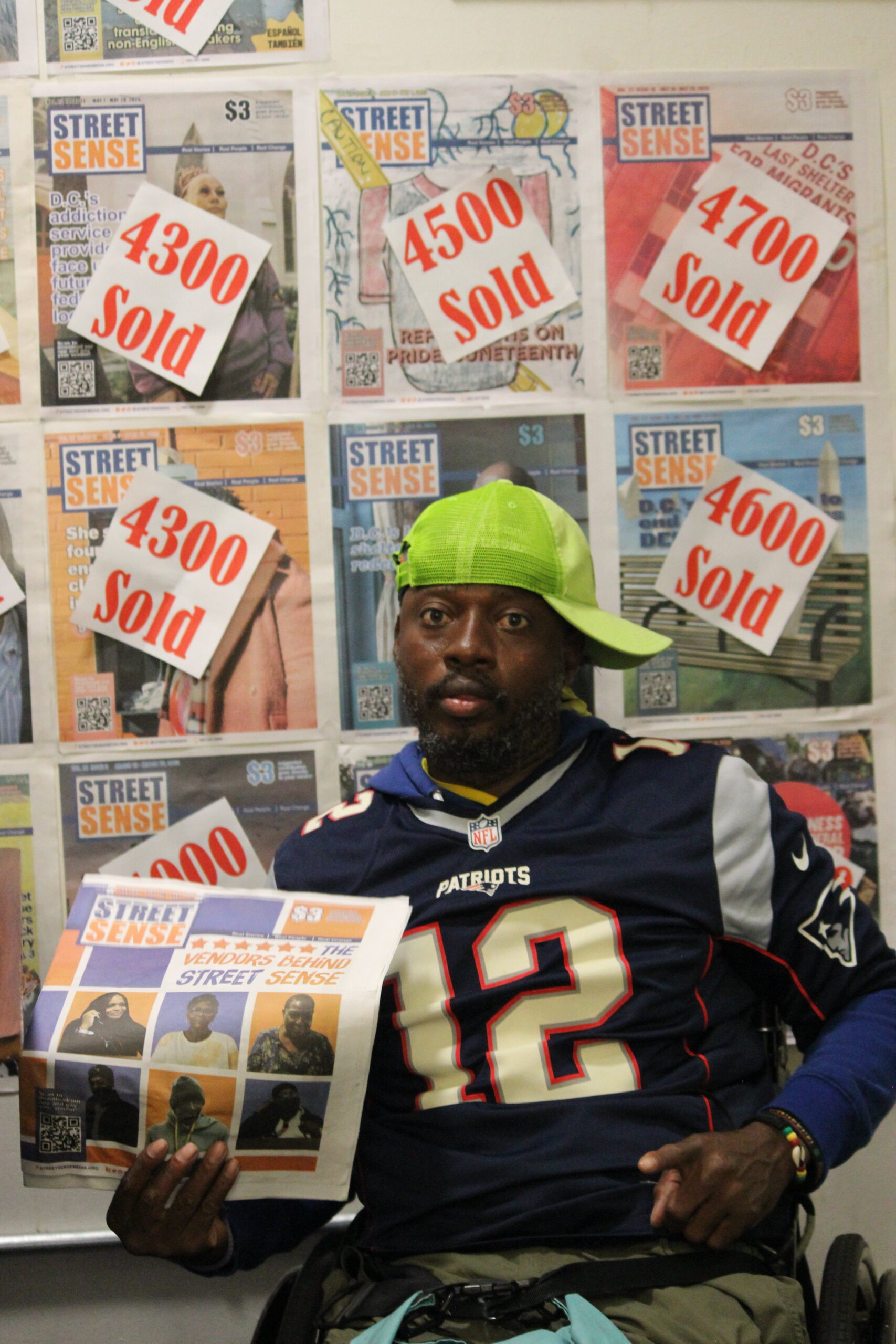 A Black man in a wheelchair poses in front of a wall of papers.